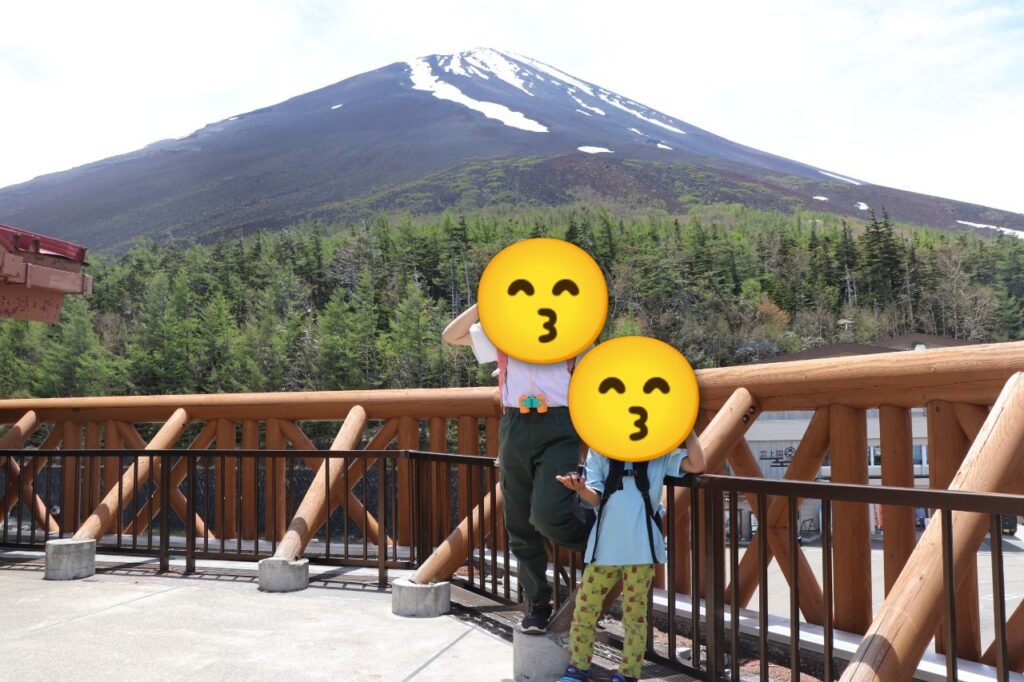 富士山五合目の展望台で、青空と残雪の富士山を背景に笑顔で並ぶ姉弟の後ろ姿（または写真）
